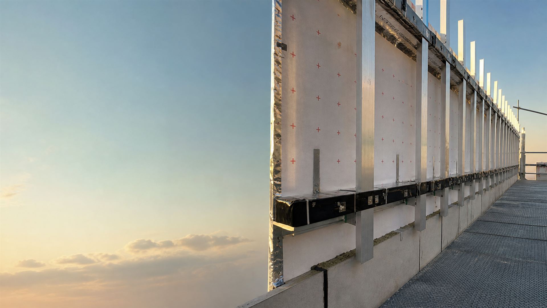High-rise facade under construction at golden hour, with cladding rails and a continuous cavity barrier line